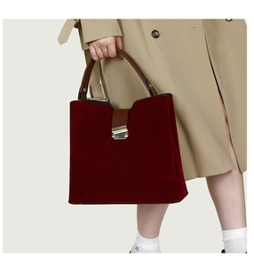 Detail of burgundy suede handbag with brown leather handles worn with a beige trench coat