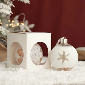 Christmas transparent glass ball with star cutout and white gift box on snowy background