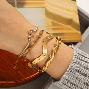 Close-up of a four-piece gold bracelet set with wavy designs and star engravings on a wrist