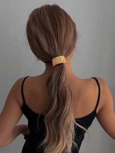 Detailed close-up of a golden textured ponytail cuff on model's hair with metallic shine