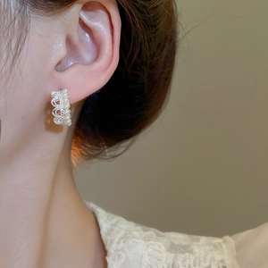 Close-up of crown shaped pearl earrings with sparkling crystals on a model's ear