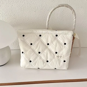 Détail d'une trousse à maquillage matelassée à pois avec base en rotin et anse