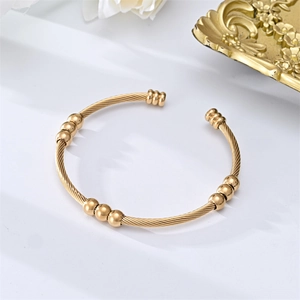 Detail of a golden C-shaped twisted cable bracelet with decorative metal beads on white background