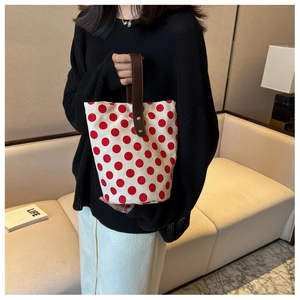 Polka dot canvas bucket bag with brown leather handle shown as a stylish handheld accessory