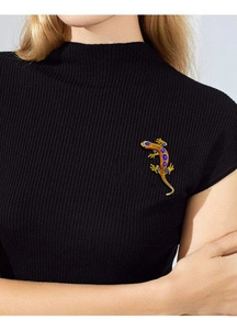 Detailed view of lizard brooch with orange enamel and blue stones on black sweater