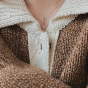 Detail of a minimalist silver key pendant necklace worn on a chunky knit sweater
