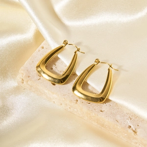 Macro di orecchini a cerchio a U in oro 18K su pietra beige e sfondo di seta crema