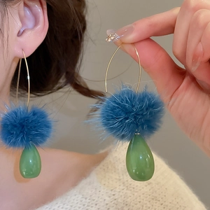 Primo piano di orecchini a goccia eleganti con pompon blu e ciondolo a goccia verde