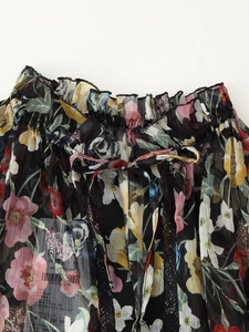 Detail of floral chiffon dress with ruffled edges and drawstring waist on black fabric