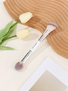 Detail of dual-ended makeup brush with white handle and soft bristles on wooden board