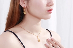 Close-up of golden MOM heart necklace and earrings set worn by a female model