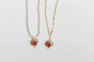 Detail of brass gold plated pearl chain and paperclip link necklace with rose enamel heart