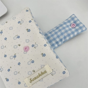 Detail of floral fabric book cover with pink snap button and blue plaid edge texture