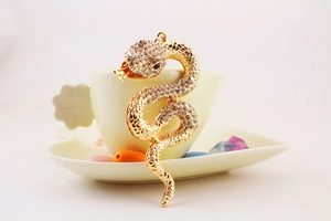 Detail of a gold snake keychain with sparkling rhinestones placed on a ceramic teacup