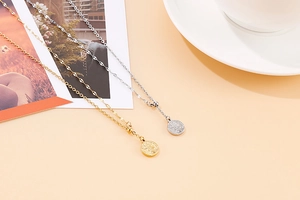 Detailed view of gold and silver stainless steel coin pendant necklaces on an aesthetic desk