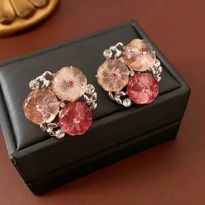 Dettaglio di orecchini a fiore sfumati rosa con strass su scatola in pelle nera