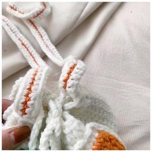 Detail van handgemaakte witte gebreide emmertas met oranje trekkoorddetails en weefseltextuur