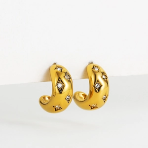 Close-up of wide gold C-shaped earrings with star-set cubic zirconia on white card