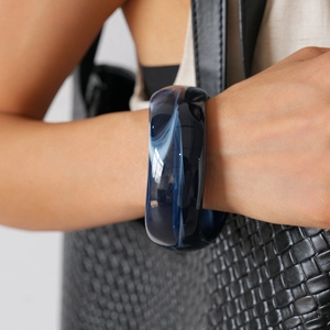 Detail of dark blue marble resin bangle with white swirls worn on wrist against black bag