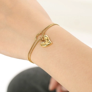 Double-layered gold heart pendant bracelet with knot detail worn on a female wrist