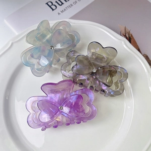 Three acetate heart claw clips in iridescent blue, grey, and purple on a ceramic plate