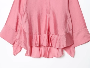 Detail shot of pink satin blouse featuring layered ruffle hem and smooth silk texture