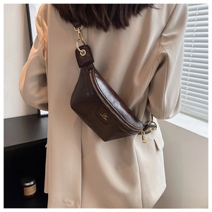 Detail of dark brown leather chest bag with gold metal logo and hardware on beige blazer