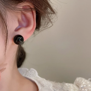 Close-up of a classic glossy black spherical stud earring on model for a minimal look