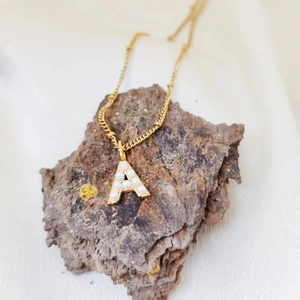 Macro view of gold stainless steel necklace featuring pearl-inlaid letter A pendant detail.