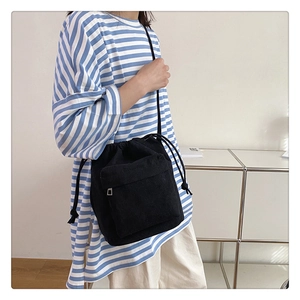 Close-up of black nylon drawstring shoulder bag styled on model with striped shirt