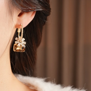 Dettaglio macro di orecchini placcati oro 18k con cristallo ambra e fiori di zircone