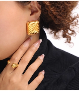 Détail de boucles d'oreilles carrées dorées texturées et bague assortie sur le mannequin