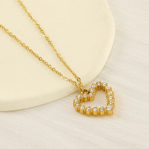 Elegant gold heart pendant necklace with shimmering crystals on a sleek white tray
