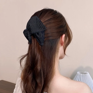 Detail view of a black polka dot bow hair clip worn in a minimalist semi-tied hairstyle