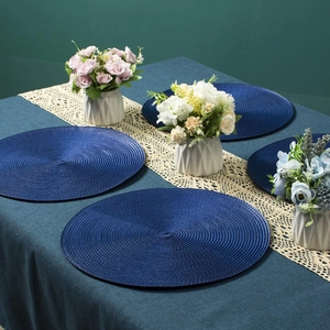 Close-up of four dark blue round braided placemats on a vintage green tablecloth