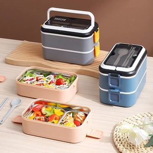 Close-up of stainless steel lunch boxes with utensils on a wooden table with salad
