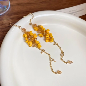 Close-up of yellow flower tassel earrings with gold chains on a white ceramic tray