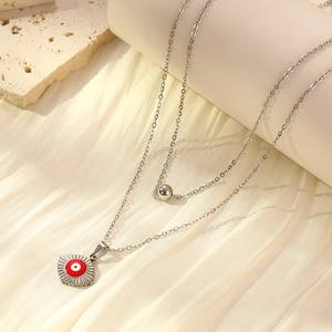 Detail of layered silver stainless steel necklace with red evil eye and silver bead charms