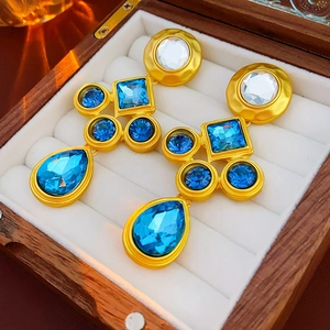 Close-up of vintage gold earrings with blue gemstones resting in a wooden jewelry box