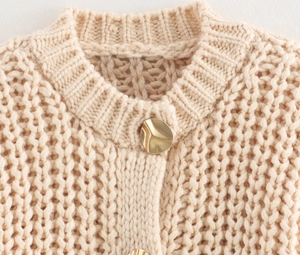 Close-up of beige chunky knit cardigan featuring a unique wavy gold metal button