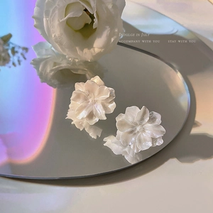 Primer plano artístico de pendientes de flores y perlas blancas sobre superficie de espejo