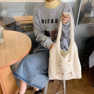Detail shot of a white fuzzy lamb wool tote bag with orange smile embroidery in a cafe