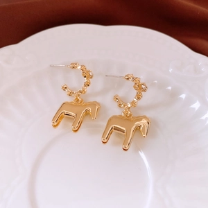 Macro shot of gold horse pendant earrings on a white embossed plate with C-shaped hoop detail