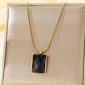 Close-up of golden snake chain with rectangular black faceted glass pendant on satin