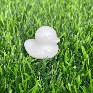 Close-up of a carved white crystal duck figurine placed on green artificial grass