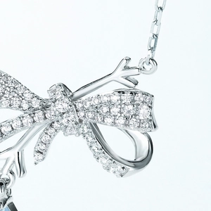 Macro shot of bow pendant with dense diamond inlay and branch texture on silver necklace