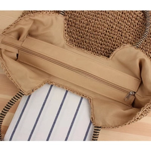 Detail view of woven straw bag showing fabric lining, metal zipper and striped handles