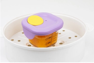 Detail of 200ml glass baby food container with purple lid and volume scale in a steamer