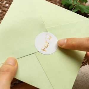 Close-up of a light green gift envelope with a golden For Ü sticker and natural background