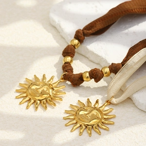 Luxurious 18K gold plated sun pendant necklace with beige ribbon on a white stone background